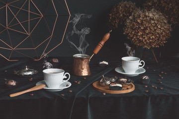 White cups with hot, smoking coffee on a black background. Around chocolate pralines.