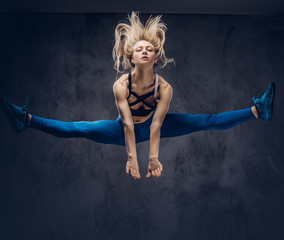 Young blonde ballerina in sportswear dances and jumps in a studio. Isolated on a dark background.