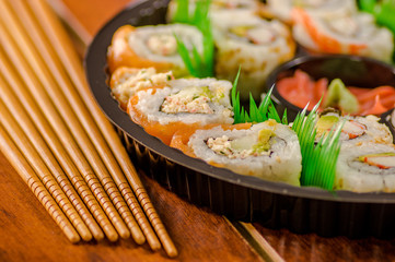Close up of selective focus of large set of delicious japanese rolls on a black plastic plate over a wooden table.