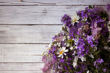 Fototapeta na wymiar Many different types of flowers: purple and violet phlox, white daisy, pink bells on a white wooden background. Place for text