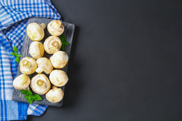 White fresh champignons with parsley on a wooden board on a gray dark table. Mushrooms. Copy the space. Top view.