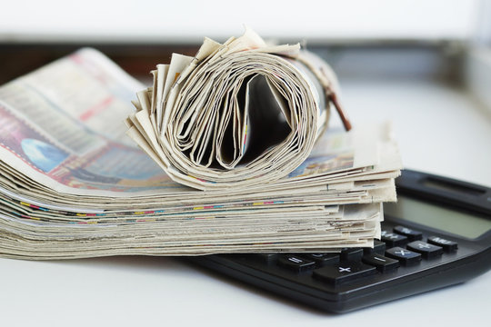 Folded and rolled newspapers and calculator. Paperwork on the desk at office. Journals with business news. Headlines and articles on tabloid pages, concept for market monitoring 