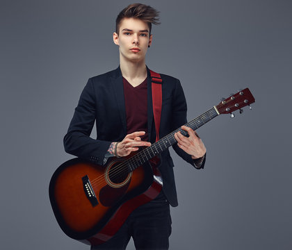 Handsome young musician with stylish hair in elegant clothes, playing on an acoustic guitar.