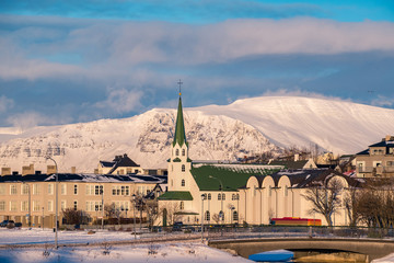Beautiful shot of Reykjavik downtown with lutheran church in a golden evening light. Capital city of Iceland Reykjavik in winter surrounded with snow covered mountains.