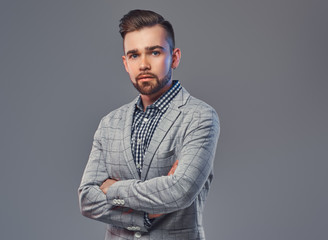 Obraz premium Handsome bearded man with hairstyle in an elegant gray jacket, posing with crossed arms in a studio, looking at a camera.