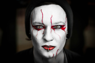 Close up portrait of young guy with piercings on his face and black-metal make up. On dark blur background. Scenic image of a musician for a concert.