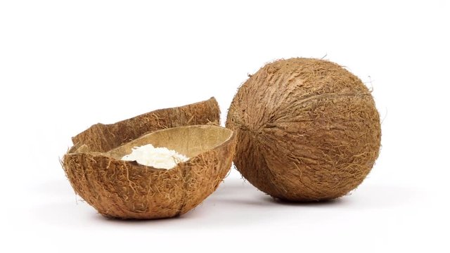 One whole and two shells halves of tropical coconut with dried white coconut flakes rotating on white isolated background. Healthy tropical fruits. Loopable seamless cocos rotating