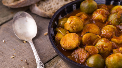 Roasted fresh brussels sprouts in homemade ceramic bowl on natural wooden background.