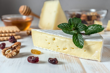 Fresh Brie cheese, Greek cheese graviera and a slice on white wooden board with nuts, honey and herbs.