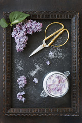 Close-up photo of beautiful fresh lilac flowers in sugar and vintage scissors in frame on black table background. Top view
