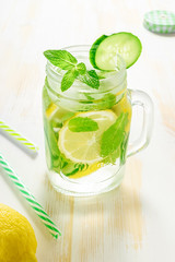 Detox water infused with sliced lemon, cucumber and sprigs of mint on wooden background.