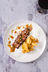 Top view grilled beef steak and fried potatoes with red wine in a glass on background, restaurant menu concept. Beautiful juicy meat on plate.