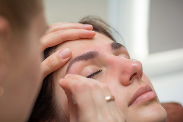 Beautiful young woman gets eyebrow correction procedure. Young woman painting her eyebrows in beauty saloon. close-up of a young woman plucking eyebrows with tweezers - obrazy, fototapety, plakaty