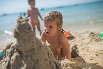 Caucasian children playing in sand on summer holiday making sand sculpture