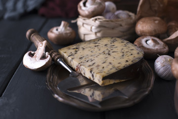 Dutch cheese, cheese knife, mushrooms, garlic and spices. Dark photo in a rustic style. Vegetarian food. Ingredients. Place for text.