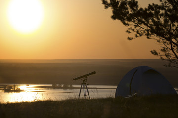 Tourist tent with telescope stands on the hill under the tree at