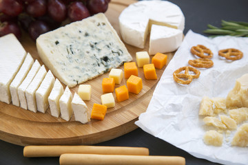 Tasting cheese with fruits, pretzels and bread sticks on dark background, Side view. Closeup.