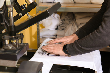 Young man printing on t-shirt at workshop