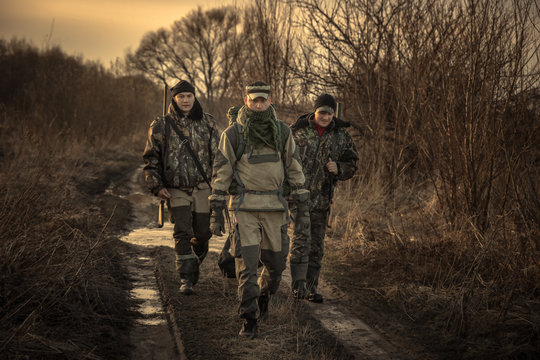 Group of men hunters with hunting equipment going on rural road hunting season sunset