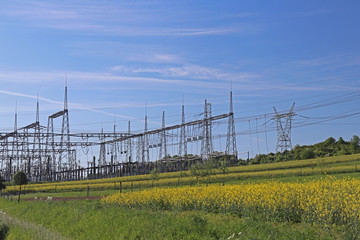 High voltage electric lines cross the hilly mestnost. Electric station in the summer under the open sky. Power industry. Ecology of nature. Metal technological structures. Strategic object at a field.