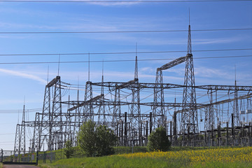 Fototapeta premium High voltage electric lines cross the hilly mestnost. Electric station in the summer under the open sky. Power industry. Ecology of nature. Metal technological structures. Strategic object at a field.