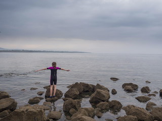 Girl in a wet suit by the ocean on cloudy day, getting ready to get into water, west coast of...