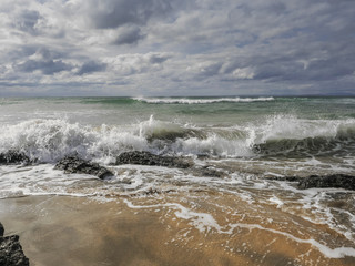 Wave hits yellow sandy beach, Blue cloudy sky over the ocean.