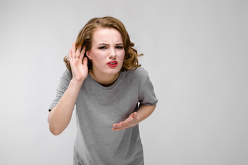 Charming young girl in a gray T-shirt on a gray background. The girl put her hand to her ear