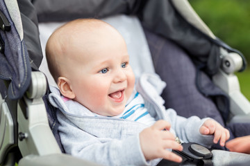 Portrait of funny baby boy laughing outdoors. Cute adorable child having fun sitting in stroller during walk
