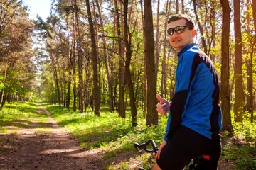 Happy young man bicyclist riding a road bike in spring forest. Man showing hand with thumb up.