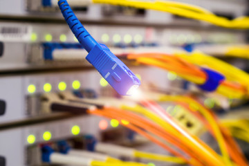 Fiber optic Patch-Cord is shown close-up in the server room of the data center. Optical Internet wire with laser light is on the background of a powerful router.