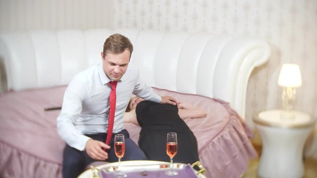 An agitated thoughtful man sitting on the bed feels sad and worried, a pensive guy looks at a drunk sleeping girl, disappointment with sexual problems, 4k