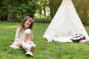 Little girl playing in a tent, children's house wigwam in park. Happy mothers day. Child with big donuts and ice cream and straw hat Summer, happy childhood concept. Cute emotions girl. © MartaKlos