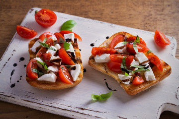 Caprese Bruschetta on white rustic chopping board. Tomatoes, basil, mozzarella cheese with balsamic sauce on toast. Antipasto - starter dish. horizontal