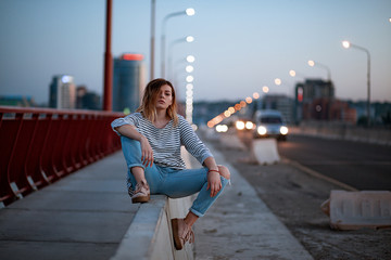 the girl is sitting on the divider near the cars on the bridge...