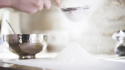 A closeup of a woman sifting a flour through a little sieve. A woman holding a little sieve to sift a flour
