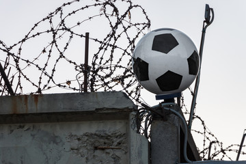 Classic soccer ball on background of concrete fence, barbed wire and barbed tape. Closed Russian football club. Bruno's spiral fence is prohibited by the Geneva Convention.