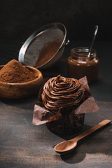 yummy chocolate cupcake with icing, cocoa powder and sieve on table