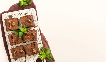  Brownie sweet chocolate dessert with walnuts and meant leaves on retro board with copy space on pastel beige background. © Yuliia Osadcha