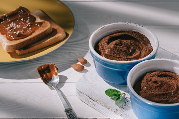 toast bread with chocolate and bowls with cocoa powder on white wooden table