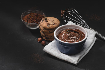 bowl with chocolate dessert, cocoa powder, whisk and cookies on tabletop