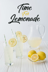 close up view of time for lemonade lettering, lemonade in glasses and jug on wooden tabletop on grey backdrop