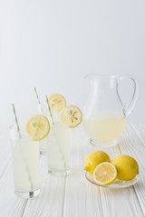 close up view of lemonade in jug and glasses with straws on white wooden tabletop on grey background