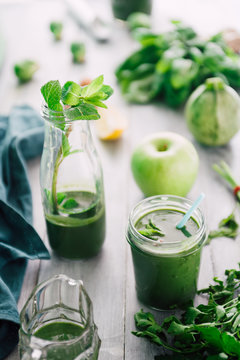 Green smoothie in bottle and  in  mason jars with apple,baby spinach, parsley and banana, on a wooden  board against a dark  background