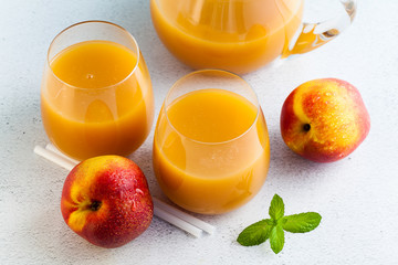 peach juice in glasses and a decanter and fresh peaches with leaves on a table. blue background. copy space