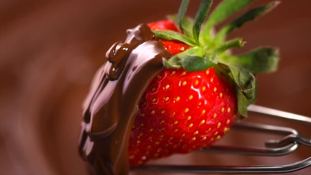 Strawberry in chocolate. Melted chocolate pouring on fresh ripe juicy strawberry closeup over swirl brown background. Fondue. Dessert. Slow motion 4K UHD video 3840X2160