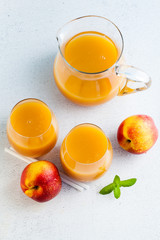 peach juice in glasses and a decanter and fresh peaches with leaves on a table. blue background. copy space