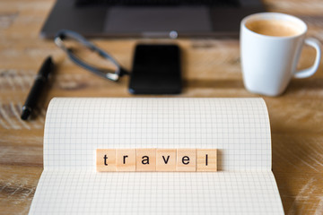 Closeup on notebook over wood table background, focus on wooden blocks with letters making Travel word