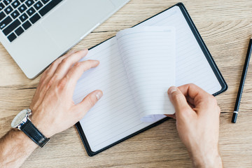 partial top view of person holding blank notebook at workplace