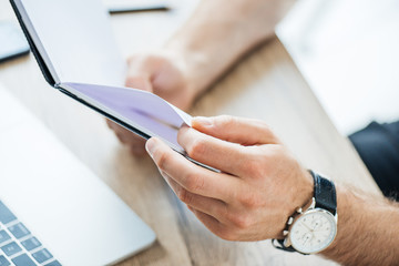 close-up partial view of male hands holding notebook at workplace